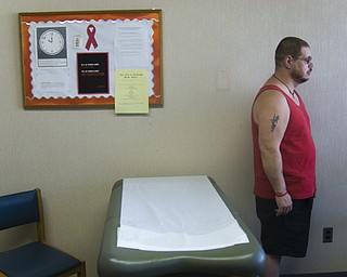 Michael Bushara, a gay, white male from Youngstown, discusses possible reasons for his lowered T-cell count with a doctor at an HIV/AIDS clinic. In the foreground is a model of dark blue HIV viruses replicating within a healthy human T-cell.