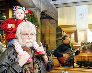 Bill Moran of West Middlesex holds his grandaughter Michaela Garltic, 1, on his shoulders during Chrsitmas at Old Mill in Mill Creek Park Sunday. In background is Roland Kausen, a Cleveland based musician who entertaining at the event.