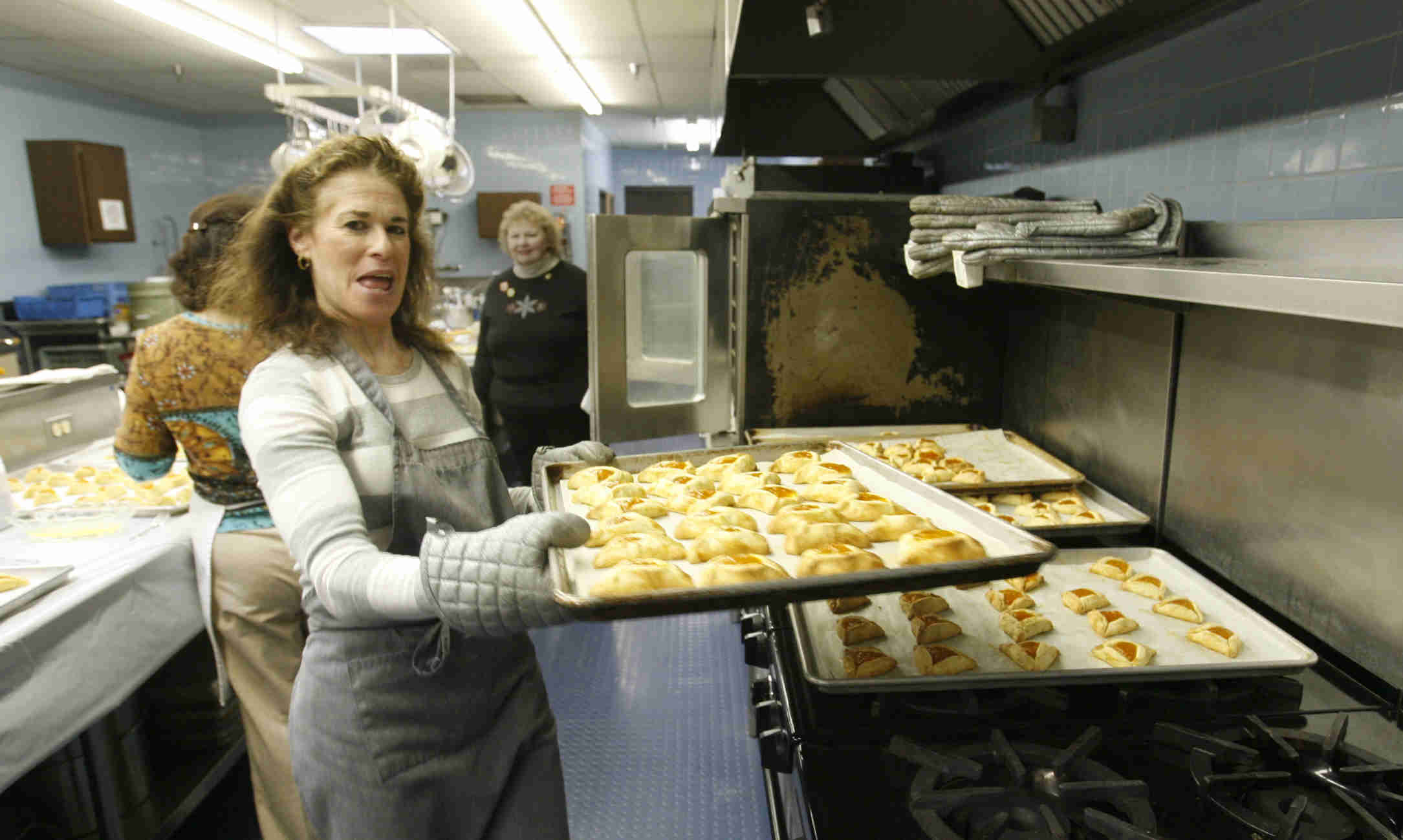Rachelle Miller pulls hot cookies out of the oven as the church makes Hamentaschen cookies for Purim- robertkyosay