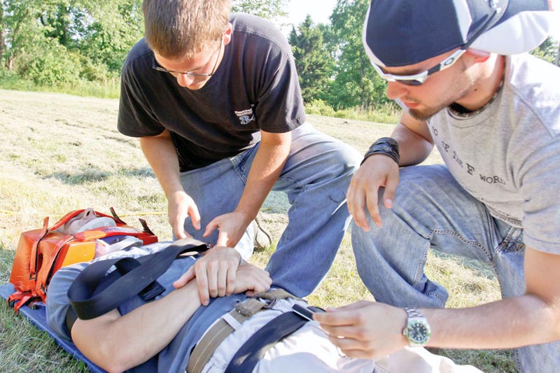 HOW IT’S DONE: Jace Melick, left, of Boardman and Brian VanDyke of McDonald strap Anthony Pilolli of Berlin Center on a stretcher as Pilolli plays the role of “patient” during an extrication exercise with Liberty Fire Department. Capt. Bill Opsitnik led the hands-on exercise for students in the emergency medical technician program at Youngstown State University.