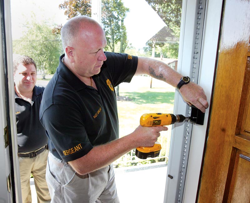 Liberty Police Department Sgt. Robert Graef installs a lock box at resident's home as part of Senior Watch Program. At left is Librty Police Capt. Toby Meloro.