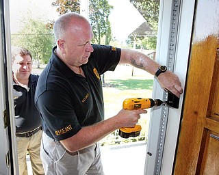 Liberty Police Department Sgt. Robert Graef installs a lock box at resident's home as part of Senior Watch Program. At left is Librty Police Capt. Toby Meloro.