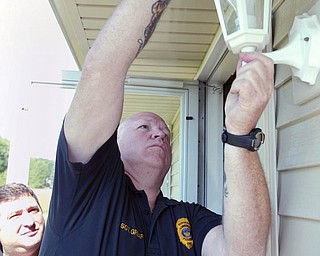 Liberty Police Department Capt. Toby Meloro, left, and Sgt. Robert Graef install a flashing light socket outside a Liberty resident's home as part of Senior Watch Program. If a resident is having a problem the resident can turn on the flashing light and officers responding can easily identify the house.