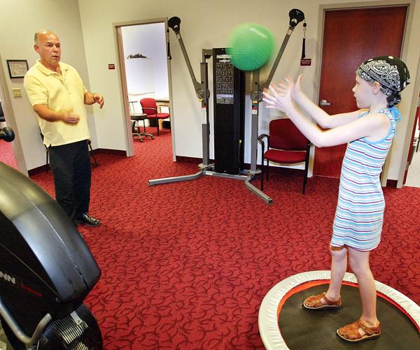 Anna Kate “Annie” Harley of Girard, who experienced a spontaneous brain bleed May 29, now is in physical, speech and occupational therapy after brain surgery on May 30. Here, Chuck Fagan, physical therapy assistant at Atlas Rehab and Wellness in Liberty, works with the 8-year-old on her coordination by tossing her a ball as she stands on a small trampoline.