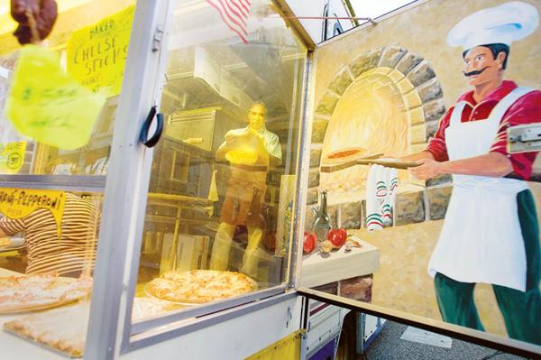 A REFLECTION OF THE PAST: Amico Colaizzi of Poland tosses pizza dough opposite a mural while inside Paisano’s Pizza Connection at the Greater Youngstown Italian Festival downtown. The festival, on six city blocks, features entertainment, games and food. It continues today.