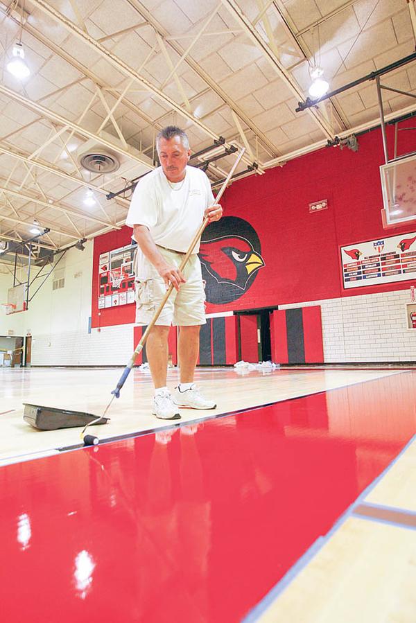 STAYING IN THE LINES: Marv Hermes, of Williams Hardwood Flooring in Akron, carefully maneuvers his paint roller along the taped lines on the new floor of Canfield High School’s gymnasium. The crew was painting the lines on the new floor Friday.