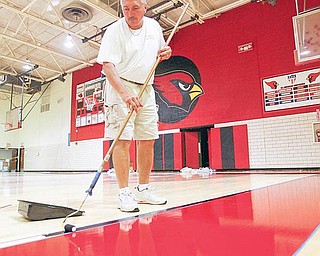 STAYING IN THE LINES: Marv Hermes, of Williams Hardwood Flooring in Akron, carefully maneuvers his paint roller along the taped lines on the new floor of Canfield High School’s gymnasium. The crew was painting the lines on the new floor Friday.