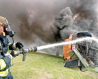 IN THE AFTERMATH: Liberty firefighter Jay Thompson waters down the undercarriage and tires of a bus set ablaze during a training exercise for firefighters and Liberty school district bus drivers. The program focused on how the two groups must work as a team in an emergency involving a school bus with students aboard.