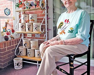 FAIR COLLECTOR: Eileen Groves, a Canfield native, sits in her home in front of a collection of 13 commemorative crocks featuring the Canfield Fair rooster mascot and slogan, “Something to crow about.” Groves now resides at Copeland Oaks Retirement Community in Sebring.