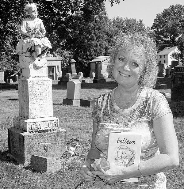 REAL-LIFE MYSTERY: Karen Biery of Salem holds a copy of her first book, “believe.” Behind her is the grave of Goldie Bell Taylor, who died in 1886. Biery was inspired to write her book because an unidentified person has been leaving flowers at Taylor’s grave in Hope Cemetery.