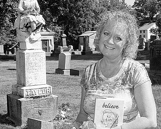 REAL-LIFE MYSTERY: Karen Biery of Salem holds a copy of her first book, “believe.” Behind her is the grave of Goldie Bell Taylor, who died in 1886. Biery was inspired to write her book because an unidentified person has been leaving flowers at Taylor’s grave in Hope Cemetery.