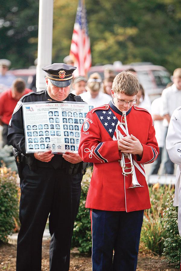 MOMENT OF SILENCE: Austintown police Officer Jeffrey Toth holds a poster with the portraits and names of all officers who lost their lives during the terrorist attacks of Sept. 11, 2001. At his side, Drew Swecker, a junior at Austintown Fitch High School, waits to play taps after a moment of silence during a memorial service Friday morning.