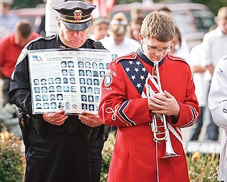 MOMENT OF SILENCE: Austintown police Officer Jeffrey Toth holds a poster with the portraits and names of all officers who lost their lives during the terrorist attacks of Sept. 11, 2001. At his side, Drew Swecker, a junior at Austintown Fitch High School, waits to play taps after a moment of silence during a memorial service Friday morning.