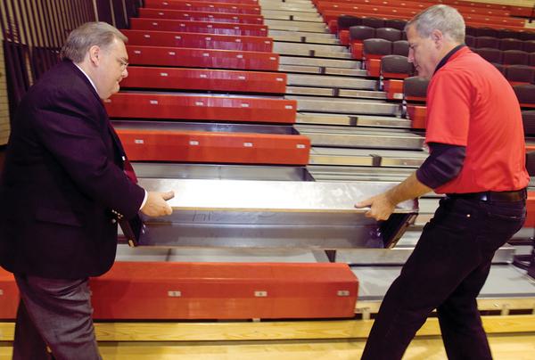 A NEW NOTION: Canfield Local Schools Superintendent Dante Zambrini, left, assists high school athletic director Greg Cooper with a removable first step to the school gymnasium’s new bleachers. The school district completed a renovation project, which cost about $300,000, and replaced the gym floor as well as the bleachers.