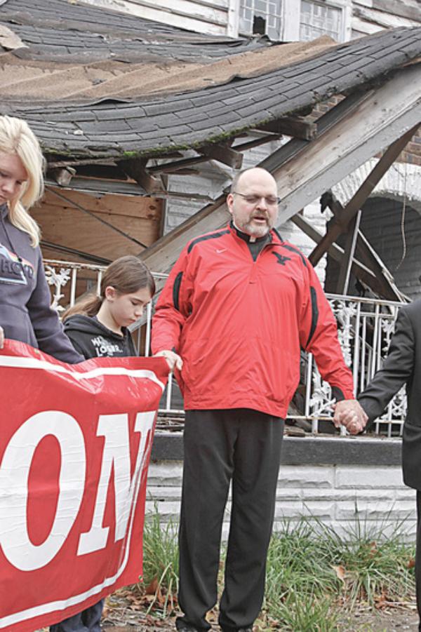 CLOSING PRAYER: Pastor Edward P. Noga, a member of ACTION, gives the closing prayer at an event in front of the former Linton Funeral Home on Youngstown’s North Side. The city will demolish the structure shortly. Holding hands with the priest are, from left, Caitlyn Cominsky, 15, and her sister, Haylee, 11, both of Youngstown.