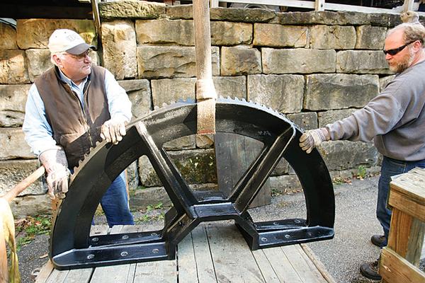 SHIFTING GEARS: Ted Lyda, left, manager of Lanterman’s Mill, and Curt Artman of Ridge Machine and Welding in Toronto, Ohio, assess two halves of the bull gear, which is placed on the water wheel of the mill. The parts, each weighing about 1,000 pounds, were delivered Monday and installed Thursday. In far right photo, the grindstone is an example of the stones used in the milling of flour by Lanterman’s Mill. 
