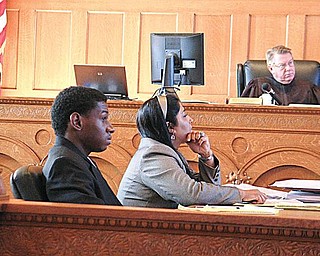 ON TRIAL: Oryan Miller, 20, of Hall Street Northwest, listens to testimony with his attorney, Sarah Kovoor, in Trumbull County Common Pleas Court. Miller is on trial in the 2008 death of Cameron Murray, 21, in Murray’s Howland apartment. In the background is Judge Andrew Logan, presiding over the trial.