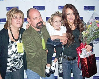 MEETING MILEY: Suzie Mazzocco of Struthers, held by her dad, Tony, gets her picture taken with her favorite singer, Miley Cyrus, before Cyrus’ Cleveland concert Sunday. At left is Suzie’s mother, Kelley.