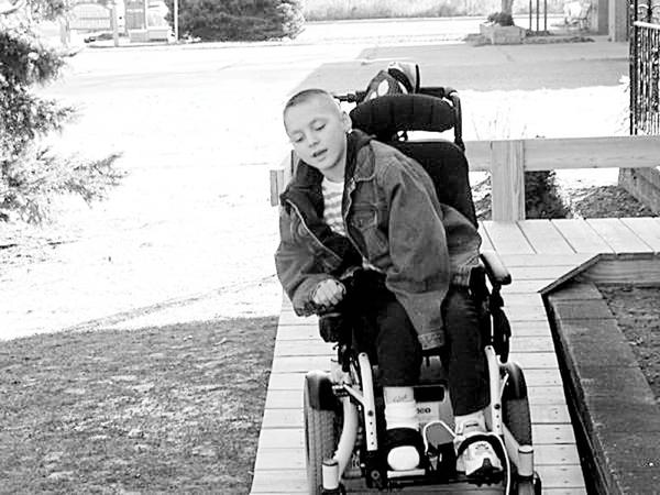 Special to The Vindicator
PRIVATE DRIVEWAY: Although his movements are limited by cerebral palsy, Tyler Wibly, a student at the Frank Ohl Intermediate School, skillfully drives his new power chair up a specially designed ramp. When it was discovered the old ramp could not handle the weight or center-wheel drive of his new chair, his parents turned to the Rotary Club of Austintown for help, and the club contacted the Optimist Club of Austintown for assistance. Materials for the ramp were purchased with funds provided by Rotary, and volunteers from both clubs were helped by Tyler’s parents as they worked together to construct the ramp.
