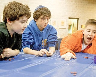 DREIDEL GAME: From left, Adam Redlich, 11, of Youngstown, Ben Feuer, 12, of Canfield and Jared Rosenberg, 11, of Youngstown wait for a dreidel to stop spinning while playing a game for beans during a Hanukkah event at Temple El Emeth in Liberty on Wednesday. Hanukkah begins at sundown today and lasts for eight days.