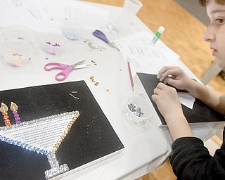 Adam Redlich, 11 of Youngstown, takes some tips from a neighbors project while constructing a sequenced menorah during a Hanukkah event with crafts, songs and games at Temple El Emeth in Liberty on Wednesday evening. Blessings said while lighting the menorah candles can be seen in Hebrew script at the center of the menorah.