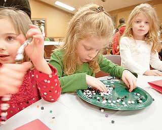 The Vindicator/Geoffrey Hauschild
Cadence Vlaiku, 4, Alizabeth White, 5, and Natalie White, 3, all from Boardman, turn their beaded ornament projects into bracelets during a Christmas event at Boardman Park's Lariccia Family Community Center on Thursday evening. The event featured ornament craft making, food, and photographs with Santa.