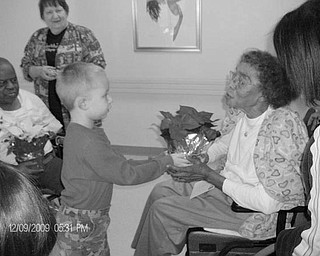 Special to The Vindicator
YOUNGSTERS GIVE GIFTS: Youngsters from the Rich Center for Autism at Youngstown State University were accompanied by parents as they delivered 50 poinsettia plants for the holidays to residents of Danridge’s Burgundi Manor at 31 Maranatha Drive. The gift giving was part of a Healing Garden Project that began this summer at the center and was financed with a $3,000 grant from the Kennedy Family Foundation. Preston Donatella, a student at the center, is shown as he presented one of the plants, supplied by Chuck’s Greenhouse in Salem, to a resident at the manor. In return for the generous gifts, staff members at the manor gave the children a huge stocking filled with toys. 