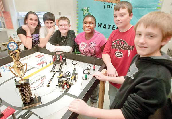 SMILES ALL AROUND: Members of the Lego Lizards of Girard Junior High School gather around the board on which “Lizzy,” the team’s robot travels. Students, from left, are Gabby Cloggins, Nick Sherock, Cameron Blenton, Jalene McClendon, Brian Spence and David Kuzman. They won the Quality Design Award in the FIRST Lego League regional competition in Canton. The trophy is at left.  