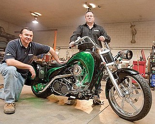 UNIQUE BIKE: Shawn Lawless, president of Lawless Industries in Boardman, stands over a hybrid motorcycle that will be shown on the “American Choppers” television show. He designed the drive system for the motorcycle. With him on the Lawless production floor is Bill Ebie of Crescent Electric Supply.