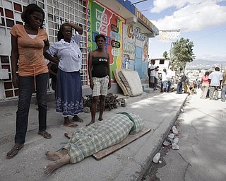 Women stand next to the body of a woman pulled from the wreckage left from the earthquake in Port-au-Prince, Wednesday, Jan. 13, 2010.