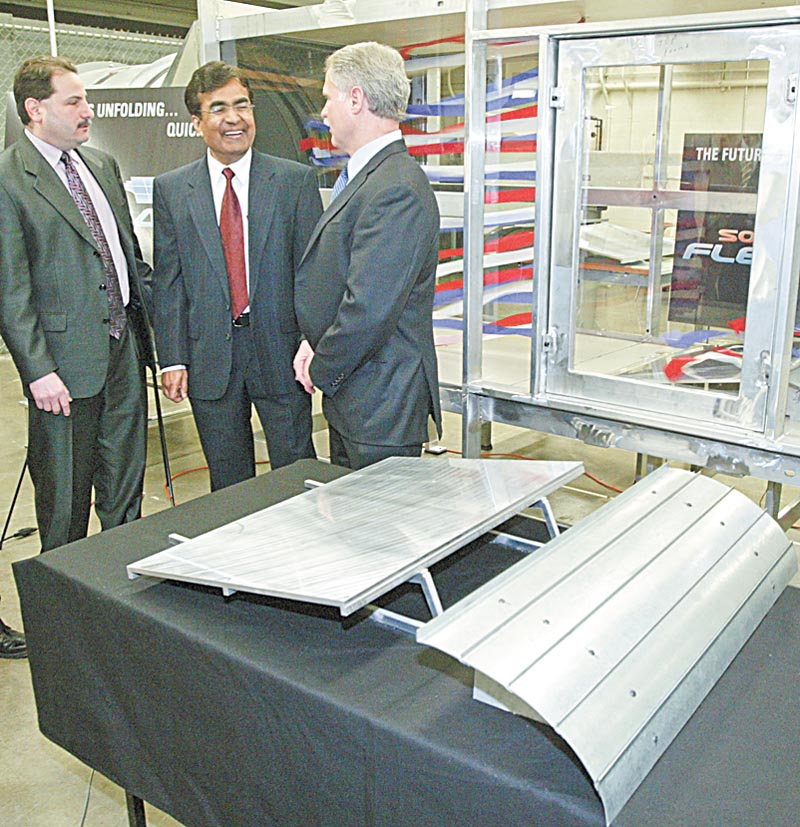 WIND TUNNEL TESTING: From left, Abraham; Ganesh Kudav, a YSU engineering professor; and Robert Voytilla, chief financial officer for Northern States Metals, discuss a wind tunnel at YSU used for testing the effectiveness of wind deflectors in the installation of rooftop solar-energy panels manufactured by Northern States. The company built the tunnel for YSU to use in the development of the deflector, a model of which is in the foreground.