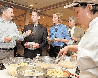 Liz Irizarry of Youngstown, right, prepares cheese tortellini as, from left, Todd Marian of Help Hotline, Scott Landy of First National Bank, Lauren Lindvig of WFMJ and Alfred J. Pasini, executive director of Youngstown Hearing and Speech Center, wait in the food line during the annual meeting of the Community Corporation, parent organization of United Way of Youngstown and the Mahoning Valley at The Lake Club, Poland.