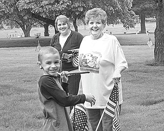 Above, Lukas Peters, a member of Cub Scout Troop 114, helps place flags on graves at Calvary Cemetery along with Jeannie Kettler, right, of VFW Post 93, and his mother, Chris Peters, who serves as den mother for the troop. Below, some members of Girl Scout Troop 977 were presented with certificates by Robert Dutton, commander of VFW Post 93 in recognition of their assistance in flag-decorating at the cemetery.