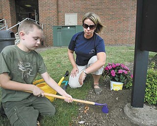 Zachary Donatella, 9, of Poland, works the ground under the guidance of teacher Vanessa Sabo outside the Rich Center for Autism. Children in the program spent time this summer in the Outdoor Healing Garden in front of Fedor Hall, Youngstown State University.