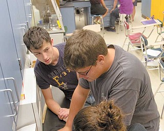 Senior Dan Miller, left, watches as juniors Nathan Stabinski and Amanda Shuluga use an analytical balance to accurately measure the mass of a piece of aluminum foil. With the mass and density, the students were able to calculate the volume of their foil, and because they already had measured the length and width of the foil, they then could find its height, or thickness.