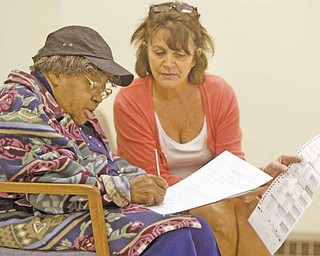 Roberta Turner of Youngstown, left, receives assistance with her early-voting ballot from Gina LaMarca, a clerk at the Mahoning County Board of Elections. Early voting started Tuesday.