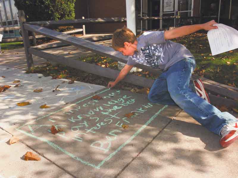 Fifth-grader Tyler Heitman outlines a quote by Benjamin Franklin on the sidewalk outside Frank Ohl Intermediate School, Austintown. Tyler was one of 400 fifth-graders at the school who participated Wednesday in National Day on Writing by chalking their favorite quotes.