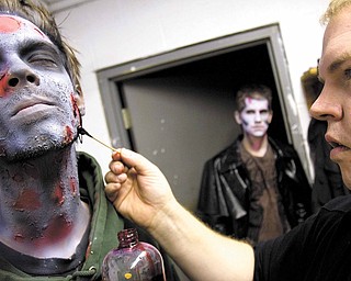 Josh Hamilton, of Salem, receives airbrushing from Joe Glenn in preparation for his zombie character whoweilds a chainsaw at the Canfield Scaregrounds on Thursday evening.