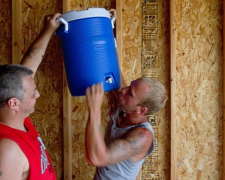 Geoffrey Hauschild|The Vindicator.7.26.2010.OVTC resident John Anderson holds up a cooler as intern Greg Todd takes a drink in Pastor Bob Pavlich's garage while working as part of a crew at nearby Arlington Heights.