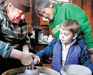 Mary Bobersky, left, of Lake Milton, a vendor at the Olde-Fashioned Christmas at the Mill crafts show, demonstrates how to shape pottery for her nephew, James Auden, 11, also of Lake Milton, and for Jackson Spin, 2, of Boardman.