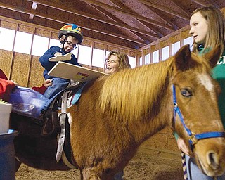 Billy Graff, 3, works to complete a puzzle during a therapeutic riding session at Forget Me Not Horse Farm in Liberty Township. He is assisted by volunteers Rachel Bowser, left, 14, of Liberty, riding instructor Penny Mulichak and Taylor Harshbarger, 14, of Girard.