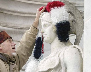 Local artist Ed Hallahan places knitted earmuffs on a sculpture outside the Butler Institute of American Art on Wednesday in preparation for the museum’s holiday show this weekend.