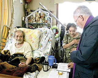 The Rev. Gerardo Hernandez, a visiting priest to St. Rosa de Lima Church in Campbell, prays with paraplegic Felix Rivera and his wife, Lourdes, in their home. Mission of Love is helping to build an addition to their house.