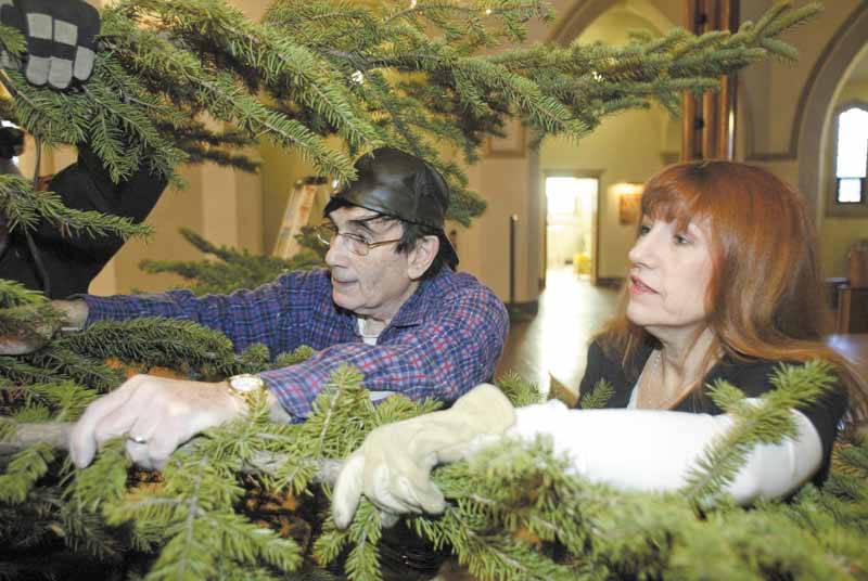 Jim Snyder and Colleen Hendel, volunteers, hang onto a bow of an 18-foot-tall blue spruce tree as its anchored in a tree holder on the altar area of St. Patrick Church on Oak Hill Avenue in Youngstown. The tree is a focal point of Christmas decor at the church.