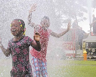 Janiyah Vogle, of Warren, and Andre Carter, 9 of Youngstown, enjoy cooling off with the help of Youngstown Fire Department's Engine 2 during the Annual African Cultural Weekend at Mill Creek Community Center on Saturday afternoon.