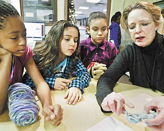Shaniya Ray, 10 (left), and Yanessa Butler, 7 (center), and Yeleysa Butler, 10, all members of the Boys and Girls club of Youngstown, watch as Katherine Bair, tutorial and enrichment director for the club, demonstrates crocheting on Monday, Dec. 27.