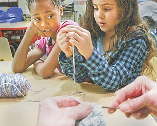 Shaniya Ray, 10, left, and Yanessa Butler, 7, both members of the Boys and Girls club of Youngstown, watch as Katherine Bair, tutorial and enrichment director for the club, demonstrates crocheting at the club Monday, Dec. 27.