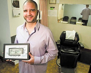 Holding the first dollar he made at his new job, Paul Gonzalez Jr., of Youngstown, stands in his barbershop on  the second floor of the Youngstown YMCA.