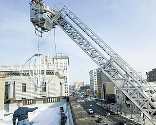 Mickey Koziorynsky, a supervisor in the Youngstown Street Department, guides the framework of the Youngstown New Year’s Eve ball onto the roof of the City Hall Annex building Wednesday at Front and Market streets downtown. The Youngstown Fire Department’s Ladder 22 was used to raise the 6-foot ball onto the roof because it didn’t fit through a third-floor stairwell. For more information on First Night Youngstown, visit www.firstnightyoungstown.org.