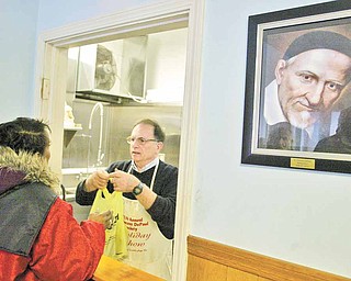 St. Vincent DePaul Society Dining Manager Skip Barone hands out a lunch at the Front Street, Youngstown location. A portrait of St. Vincent DePaul hangs on wall at right.